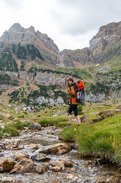 Donna con suo figlio nello zaino che cammina nei Pirenei in estate vicino a un fiume Tena Valley