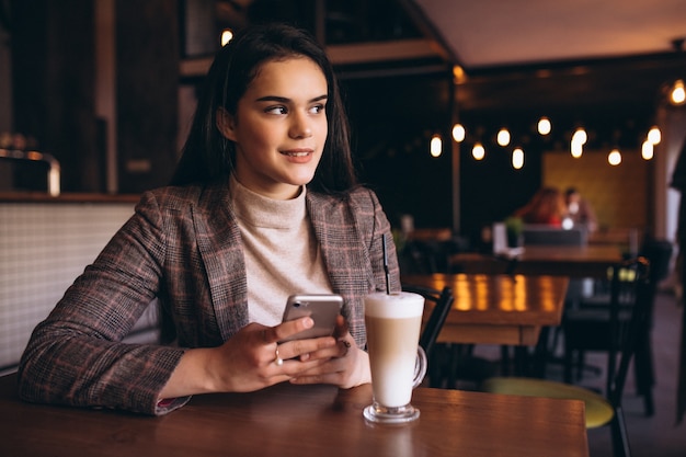 Donna con telefono e caffè in un caffè