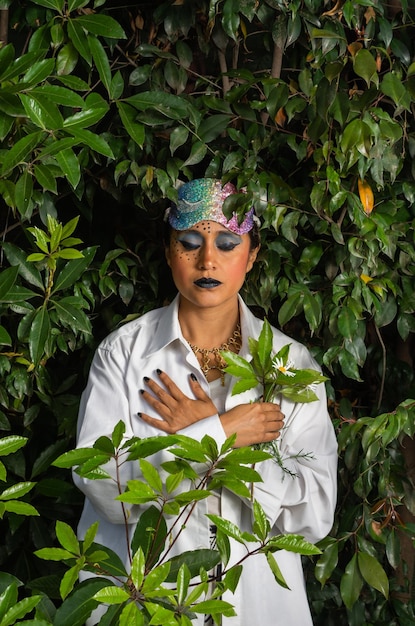 donna con trucco e maschera colorata sopra la testa e con le braccia incrociate su sfondo naturale