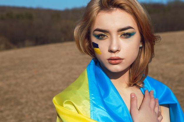 Donna con trucco patriottico avvolta nella bandiera ucraina Stand con il concetto di Ucraina