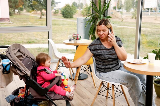 donna con un bambino in un passeggino in un caffè parla al telefono allo stesso tempo intrattiene il bambino