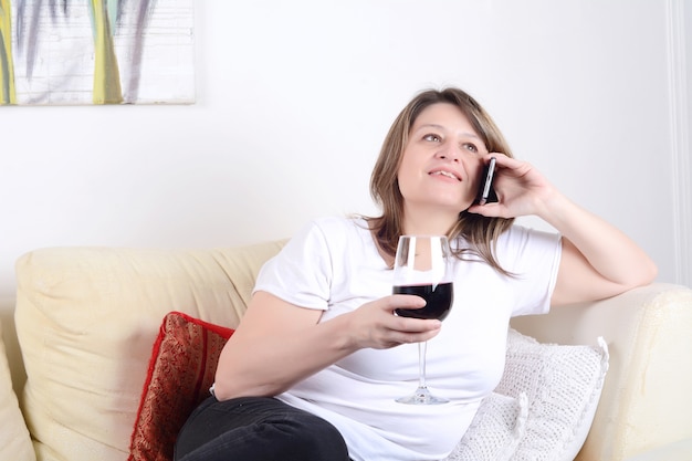 Donna con un bicchiere di vino e parlando al telefono.