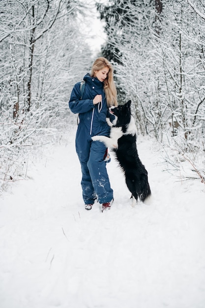 Donna con un cane border collie bianco e nero nella foresta innevata