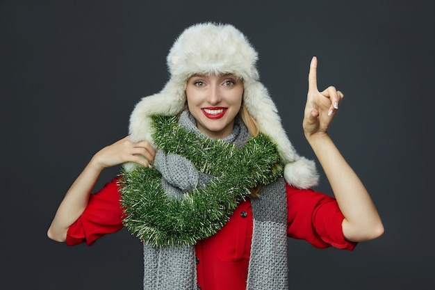 donna con un cappello invernale e decorazioni natalizie fa un gesto con il dito indice in alto sul grigio