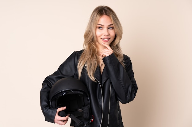 Donna con un casco del motociclo isolato sulla parete beige che osserva al lato