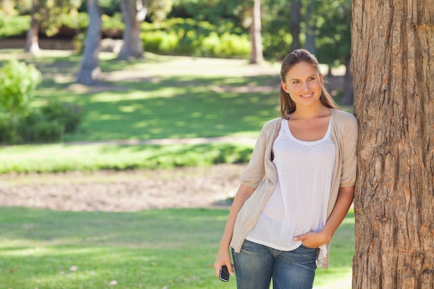 Donna con un cellulare appoggiato a un albero