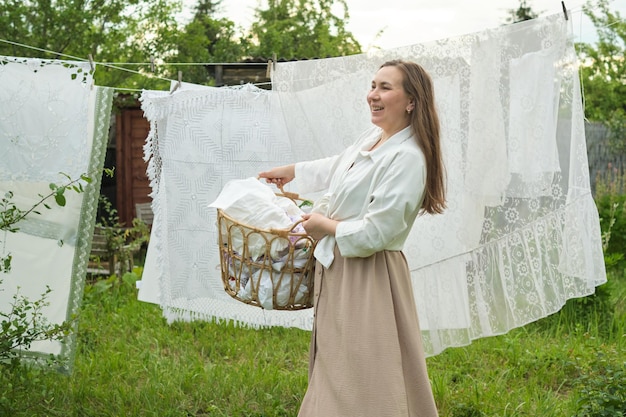 Donna con un cesto di biancheria fresca in piedi in un giardino con stendibiancheria su una linea che illustra