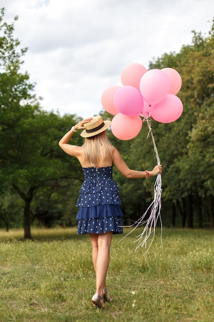 Donna con un cesto di vimini, cappello, palloncini rosa e fiori che camminano su una strada di campagna