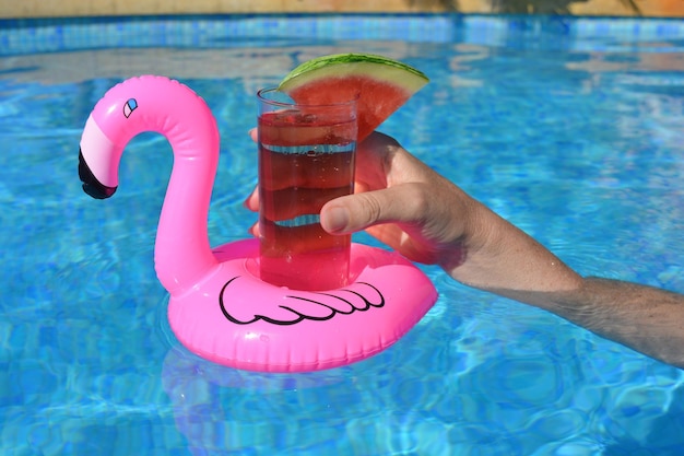 Donna con un cocktail che galleggia in un contenitore di bevande flamingo rosa gonfiabile in una piscina