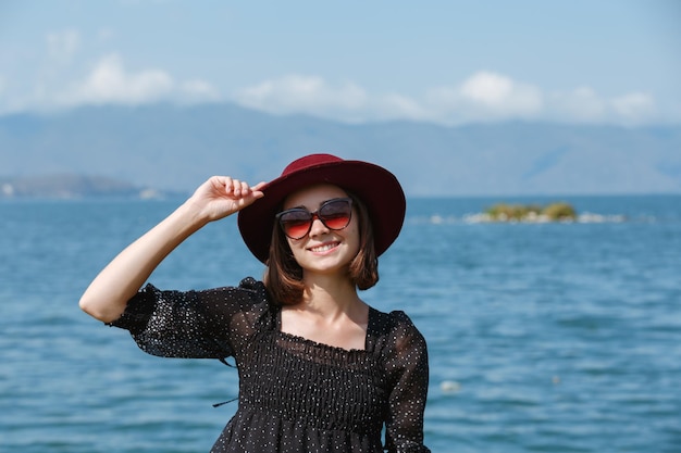 Donna con un'espressione del viso felice che tocca il cappello mentre è in piedi in abito estivo