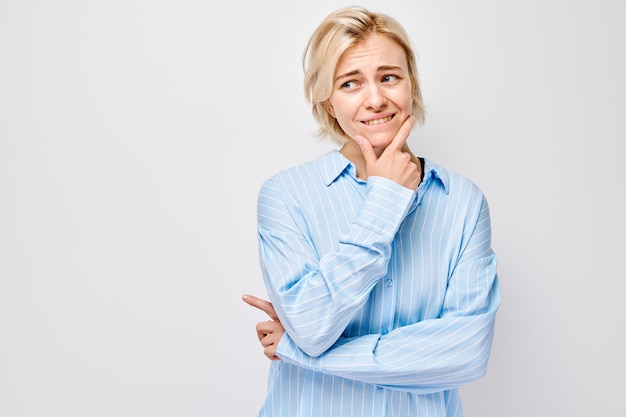 Donna con un'espressione riflessiva che tocca il mento che indossa una camicia blu su uno sfondo bianco