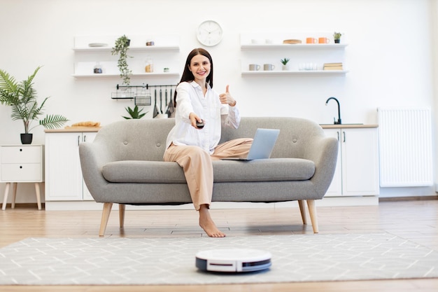 Donna con un laptop che programma il ripulimento automatico del pavimento della stanza