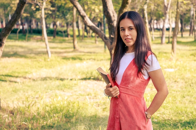 Donna con un libro che cammina nel parco con alberi sullo sfondo