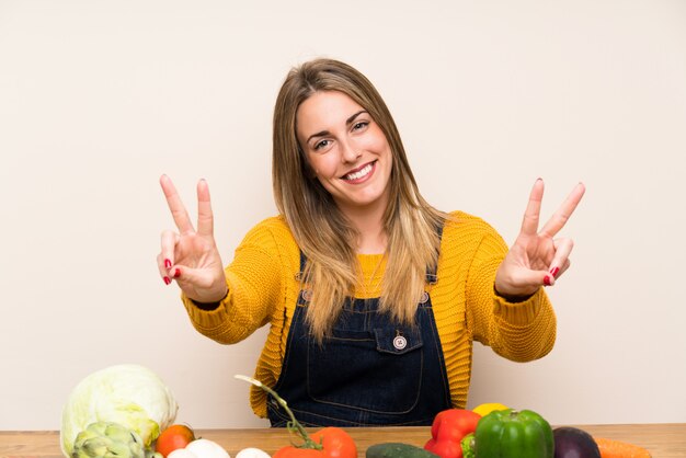 Donna con un sacco di verdure sorridenti e mostrando il segno della vittoria