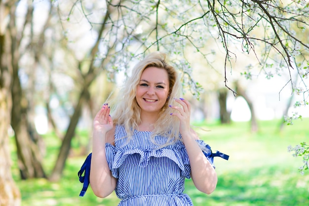 Donna con un sorriso splendido divertirsi nel giardino fiorito. Femmina in abito blu su sfondo naturale.