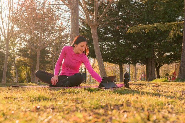 Donna con un tablet che esegue esercizi di yoga in un parco al tramonto