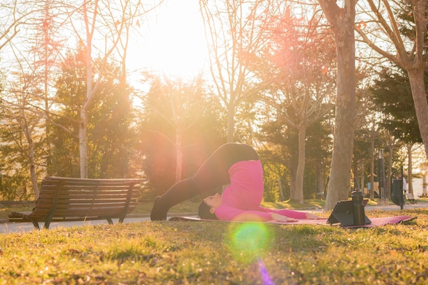 Donna con un tablet che esegue esercizi di yoga in un parco al tramonto