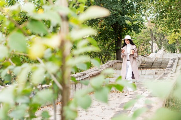 donna con un telefono e una tazza di caffè passeggia nel parco, filmata con una telecamera nascosta