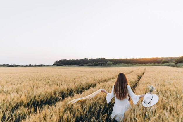 donna con un vestito bianco e un cappello bianco in un campo di grano