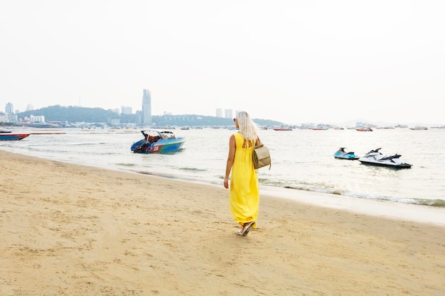 Donna con un vestito giallo che cammina a piedi nudi sulla riva del mare in Thailandia