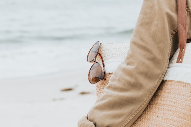 Donna con una borsa per il sole e un paio di occhiali da sole in spiaggia, copia spazio, vacanza e concetto di vacanza