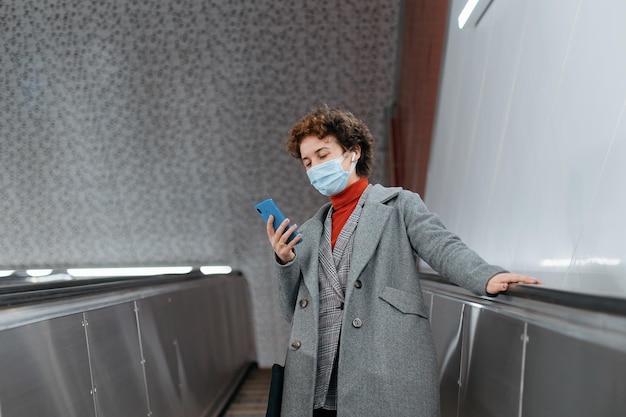 Donna con una maschera protettiva in piedi sui gradini della scala mobile della metropolitana