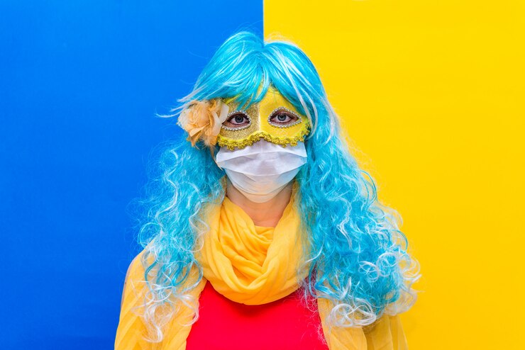 donna con una parrucca blu e una maschera di carnevale gialla, con indosso una mascherina medica della corona di virus