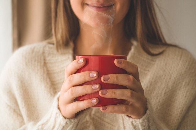 Donna con una tazza di bevanda calda vicino alla finestra. Buongiorno con il tè. Autunno Inverno