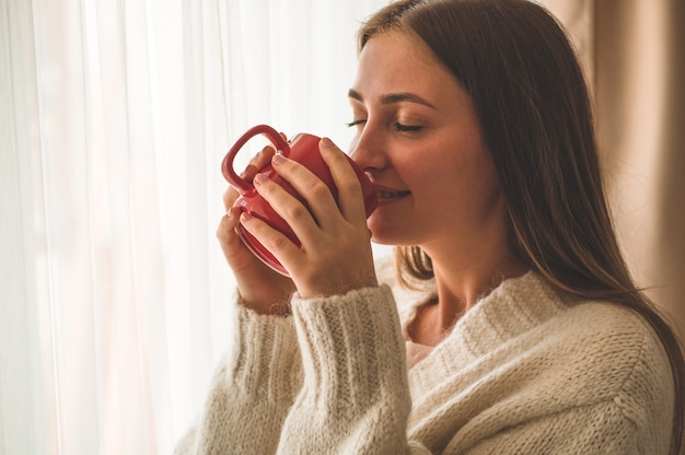 Donna con una tazza di bevanda calda vicino alla finestra