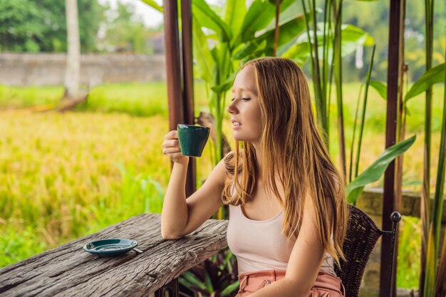 Donna con una tazza di caffè sulla veranda del caffè vicino alle terrazze di riso a Bali, Indonesia.