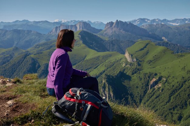 Donna con zaino in cima a una collina con paesaggio di montagne donna seduta sull'erba con vista sulle montagne