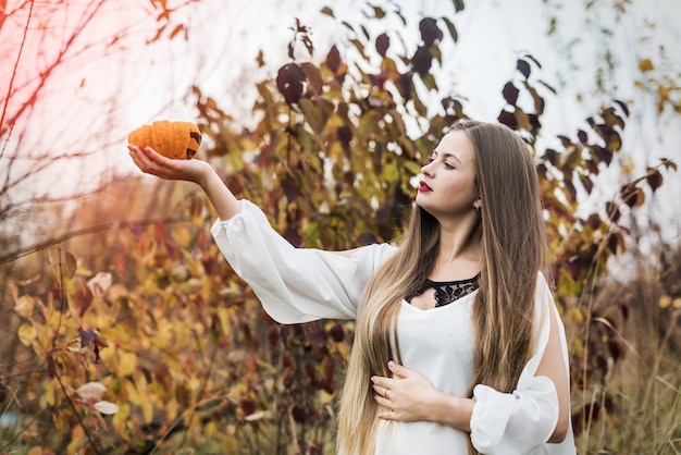 Donna con zucca arancione in posa vicino agli alberi d'autunno