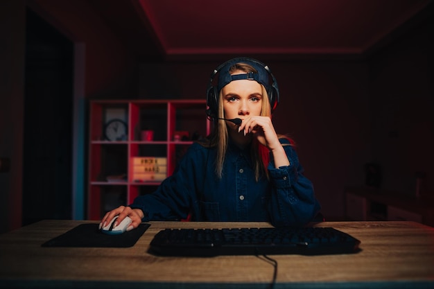 Donna concentrata in abiti casual e auricolare seduto al tavolo e giocando a giochi per computer