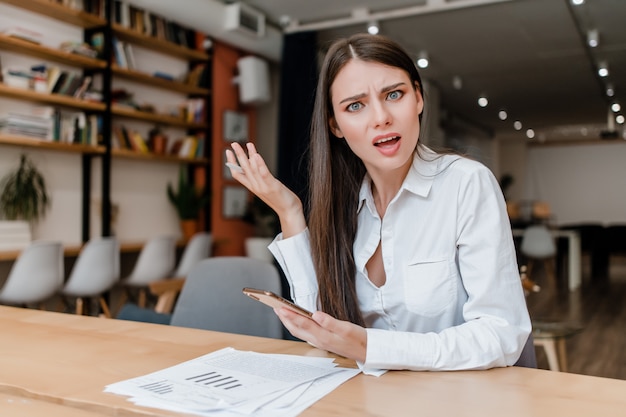 Donna confusa in ufficio con telefono e documenti