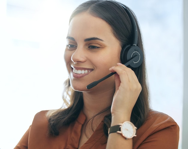 Donna consulente con auricolare e sorriso alla scrivania nel suo ufficio sul posto di lavoro Telemarketing o servizio clienti di call center o supporto e felice lavoratrice con comunicazione online con il cliente