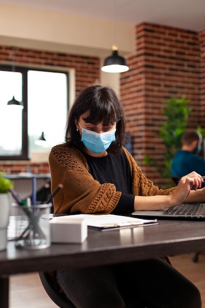 Donna contabile con maschera protettiva medica contro il covid19 che analizza la strategia aziendale che controlla il rapporto aziendale. Donna d'affari che lavora al progetto di marketing nell'ufficio di avvio