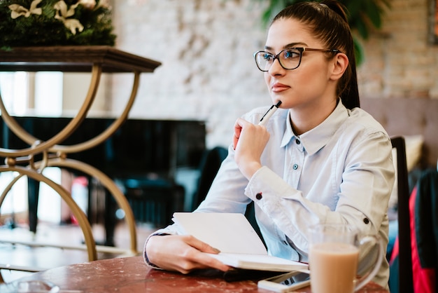 Donna contemplativa che pensa all&#39;idea per il progetto. Prendere appunti nel caffè.