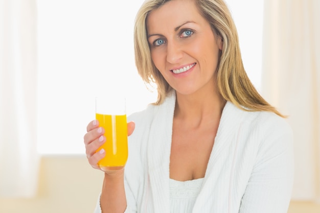 Donna contenta che guarda l&#39;obbiettivo godendo un bicchiere di succo d&#39;arancia