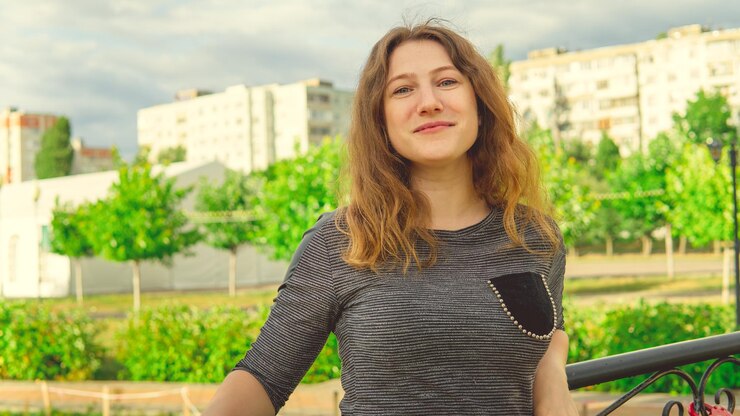 Donna contenta che guarda sognante in piedi nel parco verde contro il recinto di ferro ornamentale Donna timida appoggiata sulla maniglia in giardino