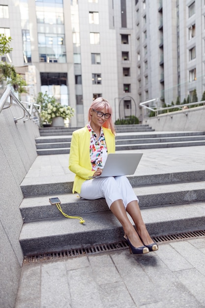 Donna contenta che lavora con il computer portatile sulle scale della città