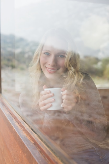 Donna contenta con la tazza di caffè che guarda fuori attraverso la finestra