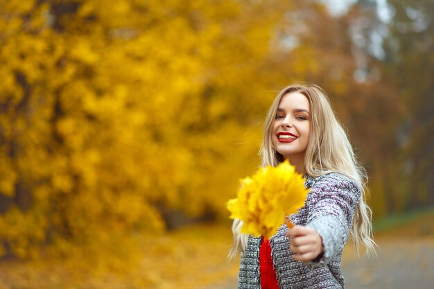 Donna contenta con le labbra rosse che tengono le foglie gialle nella foresta autunnale