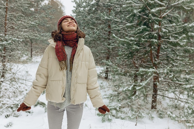 Donna contentissima in capispalla che gode di tempo nevoso nella foresta invernale