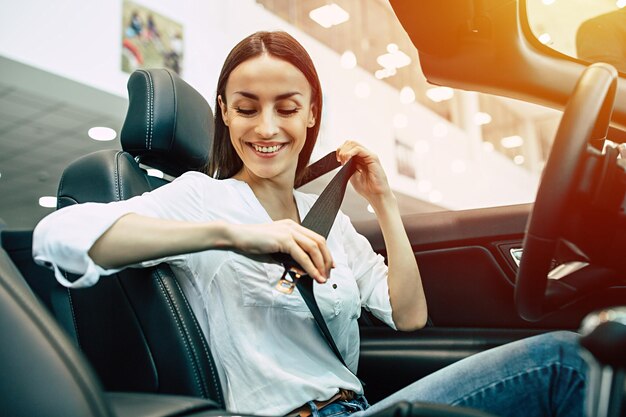 Donna controllare le cinture di sicurezza in auto Donna splendida che acquista una nuova auto per lavoro e viaggiare in concessionaria ragazza cliente