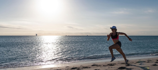 Donna correre e saltare sulla spiaggia del mare Corridore donna attiva in abbigliamento sportivo correre sulla spiaggia di sabbia lungo il mare in esecuzione