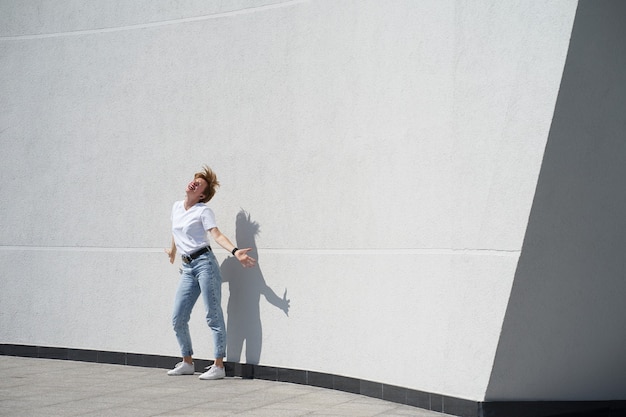 Donna corta dai capelli rossi che balla davanti a un muro bianco