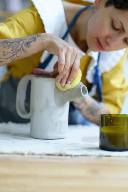 Donna creativa che modella la brocca di argilla in studio artista femminile con tatuaggi lavora su ceramica in officina