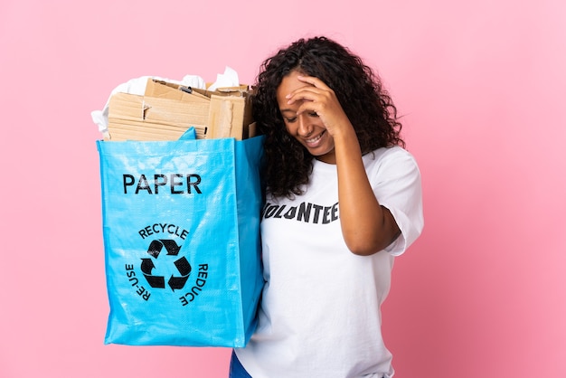 Donna cubana che tiene un sacchetto di riciclaggio pieno di carta da riciclare isolato sulla risata rosa