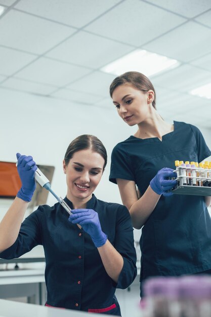 Donna curiosa in piedi con il portaprovette e guardando il suo collega usando un distributore automatico di pipette