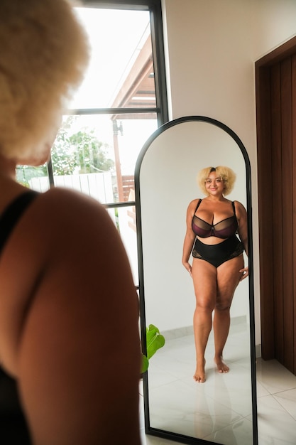 donna curva afroamericana di taglia plus in piedi davanti allo specchio che guarda il riflesso